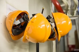 Three yellow hard hats hanging up in a white warehouse