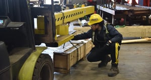 Sullivan Steel warehouse operator in a yellow hard hat adjusting chains around a wood crate