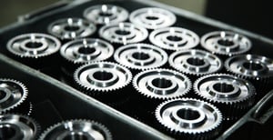 Precision-machined stainless steel gears in a metal bin.